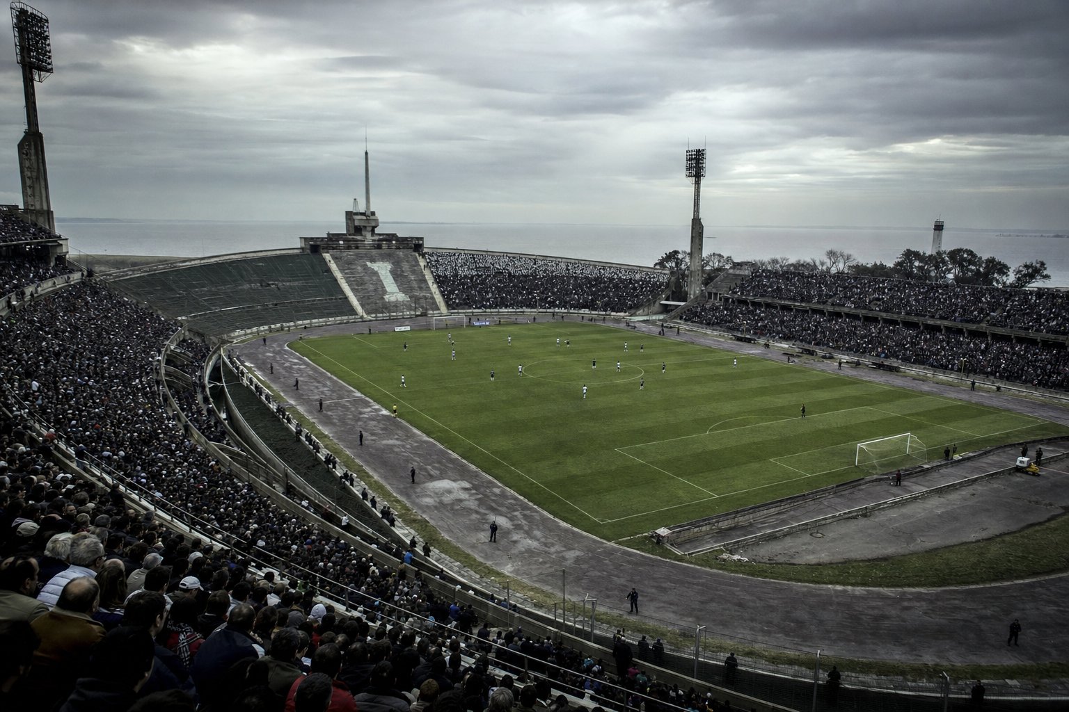 Estadio de fútbol montevideano en una tarde gris, con las tribunas llenas frente al río